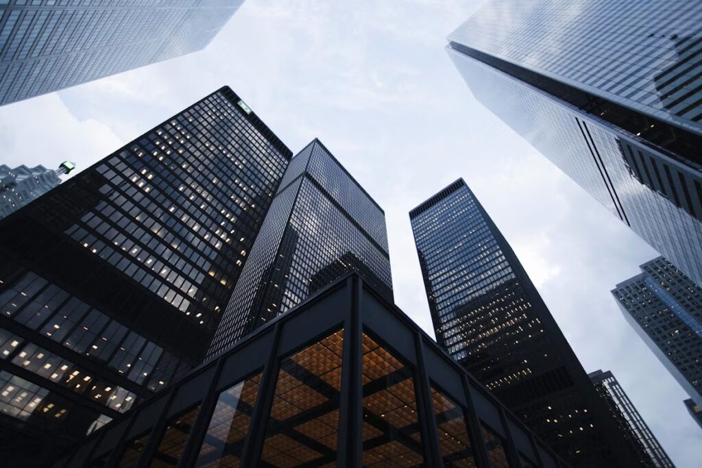 Several tall office buildings and finance skyscrapers with glass facades are viewed from street level against a cloudy sky.