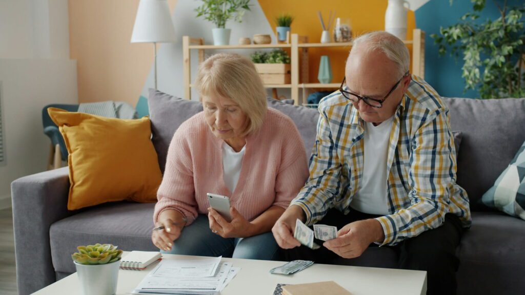 Older couple reviewing bills and cash together at home using a smartphone